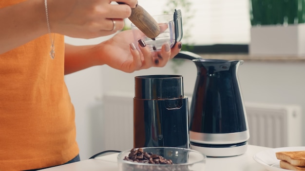 コーヒーグラインダーを使用して朝食用の淹れたてのコーヒーを作ります。自宅で主婦が朝食、飲酒、仕事に行く前にコーヒーエスプレッソを挽くためにキッチンで挽きたてのコーヒーを作る