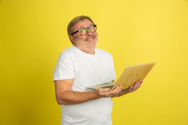 Используя ноутбук, улыбаясь. Портрет кавказского человека, изолированные на желтом фоне студии. Красивая мужская модель в белой рубашке позирует.
