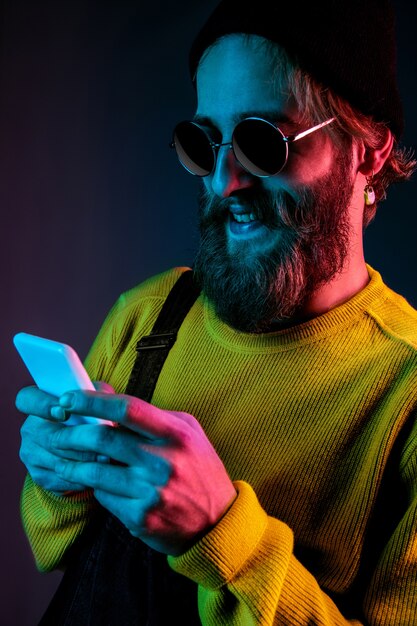 Using phone in sunglasses. Caucasian man's portrait on gradient  space in neon light