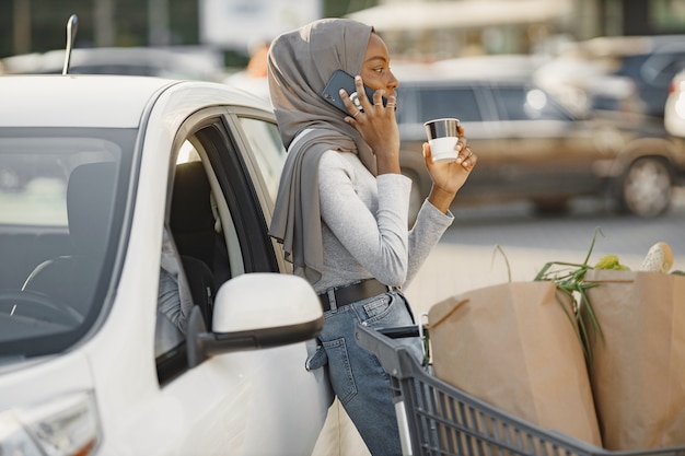 Using smartphone while waiting. African ethnicity woman on the electric cars charge station at daytime. Brand new vehicle.