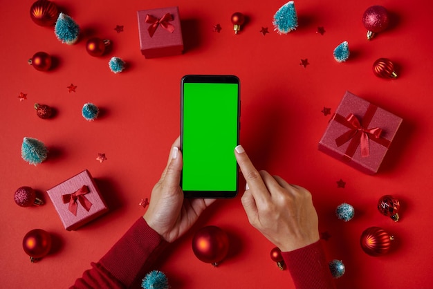 Using Smartphone with blank green screen on table with Christmas decorations Top view