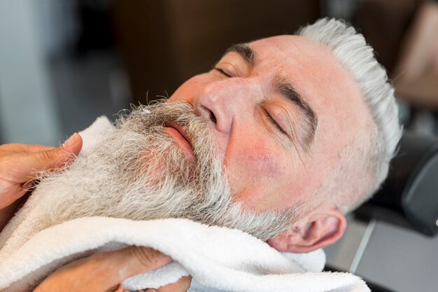 Using towel on beard of aged male in barbershop