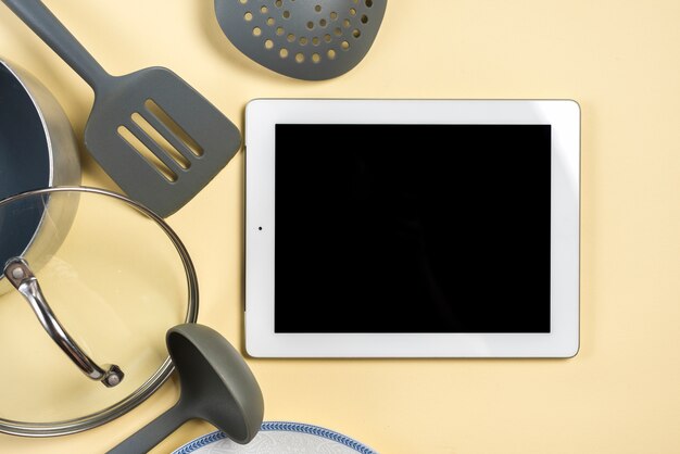 Utensil; spatula; ladle and black screen digital tablet on beige background