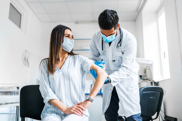 Vaccination. The doctor in a protective mask and gloves injects the vaccine into the patient's hand.