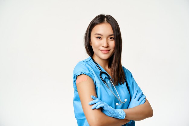 Vaccination and medical workers concept. Confident nurse, asian female doctor with vaccinated hand, cross arms on chest and smiling, white background