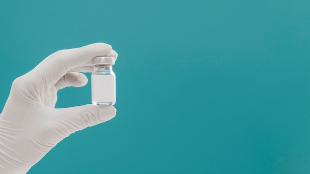 Бутылка вакцины, удерживаемая рукой с перчаткой и копией пространства