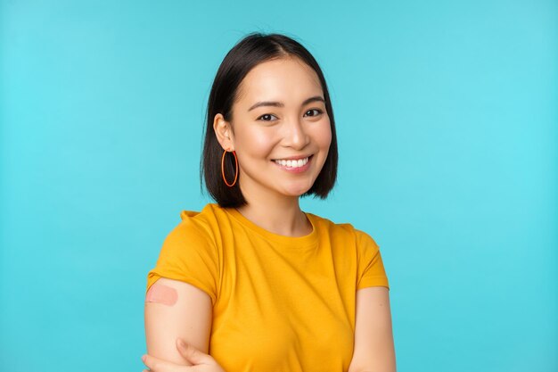 Кампания по вакцинации от covid19 Молодая красивая здоровая азиатка показывает плечо с забинтованной концепцией вакцинации, стоящей на синем фоне