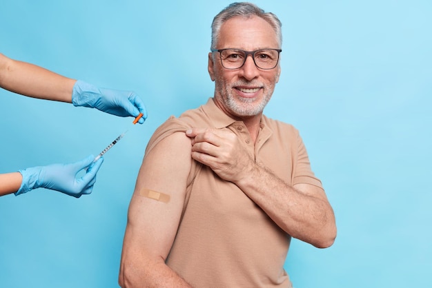 Vaccine injection against coronavirus Pleased old man being immunized against covid 19 at hospital during visit to doctor isolated over blue wall wears plaster on arm Vaccination for elderly people
