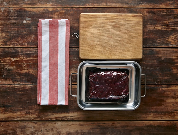 Confezione sottovuoto di pentola in metallo bistecca di carne di balena con asciugamano e piatto di legno, vista dall'alto