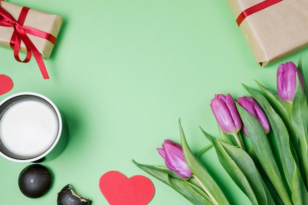 Valentine background with gift box sweet hearts and tulips on green table Top view flat lay