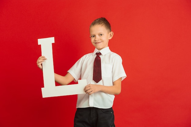 Valentine's day celebration. Happy, cute caucasian boy holding letter on red studio background.