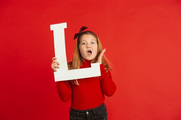 バレンタインデーのお祝い、赤いスタジオの背景に手紙を保持している幸せでかわいい白人の女の子。