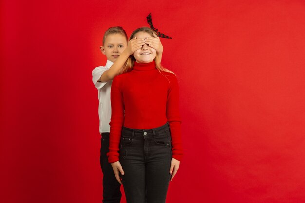 Valentine's day celebration, happy, cute caucasian kids isolated on red studio
