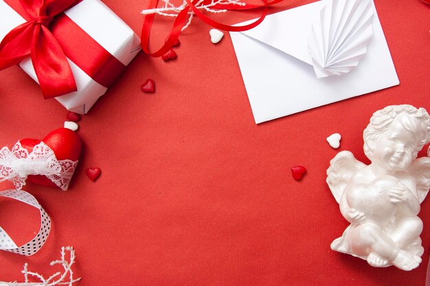 발렌타인의 날은 빨간색 배경에 평평하게 놓여 있습니다. 봉투, 선물, 심장, 천사, 리본. 텍스트를 위한 여유 공간입니다.