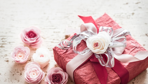 Foto gratuita il giorno di san valentino e la festa della mamma, confezione regalo rossa con fiocco e rose su fondo in legno chiaro