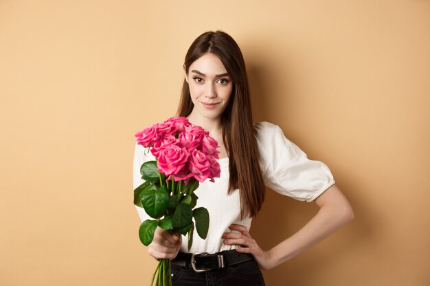 Valentines day beautiful girlfriend holding pink roses and looking at camera young woman receive flo...