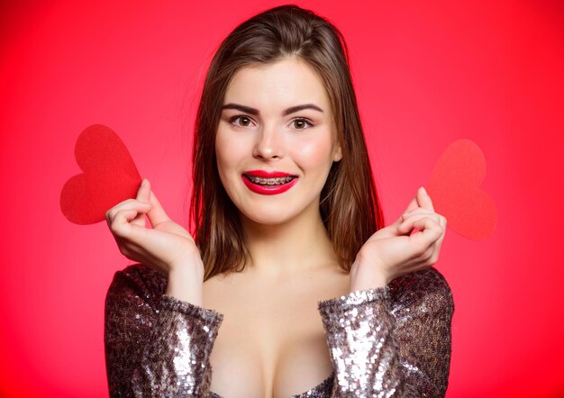 Valentines day concept. braces and beauty. dating when you have adult braces. girl pretty wearing orthodontic braces and smiling. how to kiss with braces. woman makeup red lips hold heart symbol love.