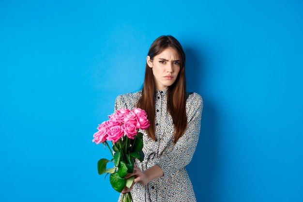 Valentines day concept displeased young woman rejecting flowers gift frowning and grimacing refusing...