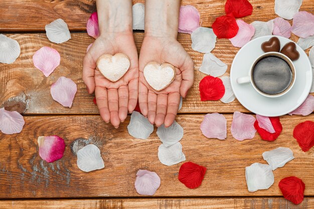 Valentines Day concept. Female hands with hearts on wooden with flower petals and cup of coffee
