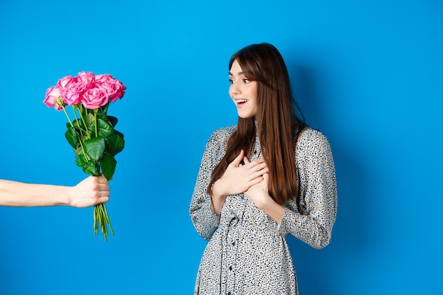 Valentines day concept image of surprised beautiful girl looking at hand with bouquet of flowers rec...