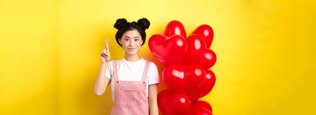 Concetto di giorno di san valentino elegante ragazza asiatica adolescente con trucco romantico sguardo tenendo le dita incrociate