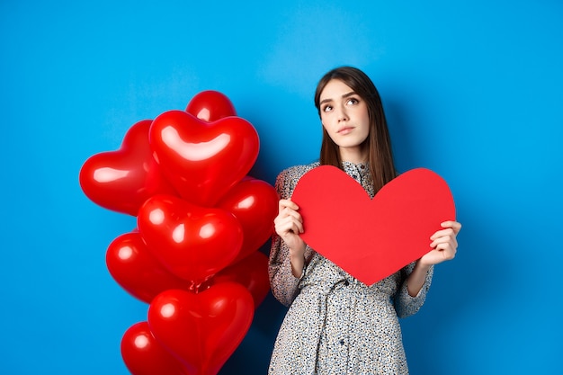 Free photo valentines day dreamy pretty lady in dress holding big red heart cutout and searching for true love ...
