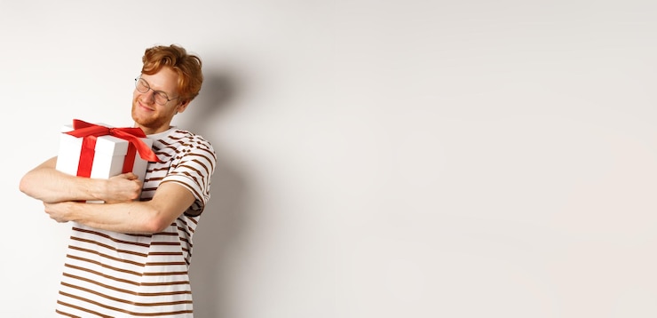 Free Photo valentines day and holidays concept happy redhead man hugging his gift box and smiling delighted sta