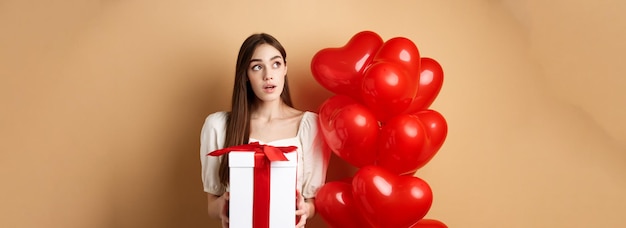 Free photo valentines day pensive cute girl guessing who made her gift holding present and looking curious at u