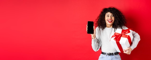 valentines and lovers day excited smiling woman with curly dark hair showing smartphone empty screen