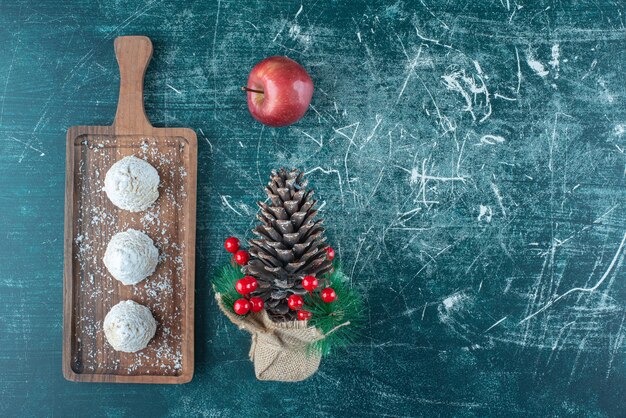 Free photo vanilla-coated cakes on a small tray, an apple and a christmas ornament on blue.