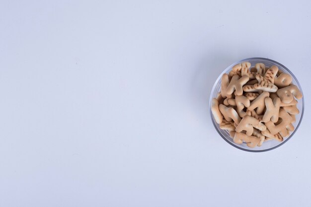 Vanilla crackers in letter shape in a glass cup on blue.