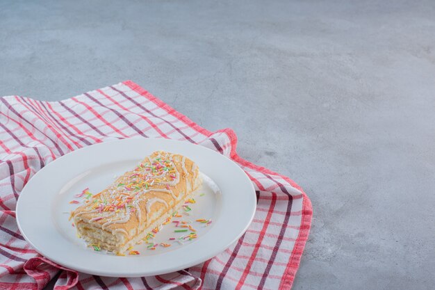 Vanilla flavored sweet roll decorated with sprinkles on white plate.