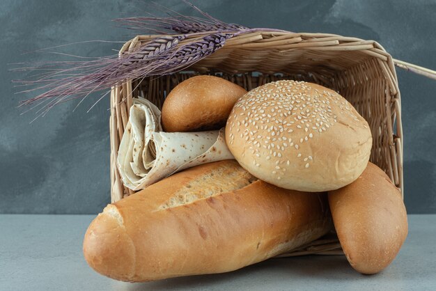 Variety of bread in basket and wheat on stone surface