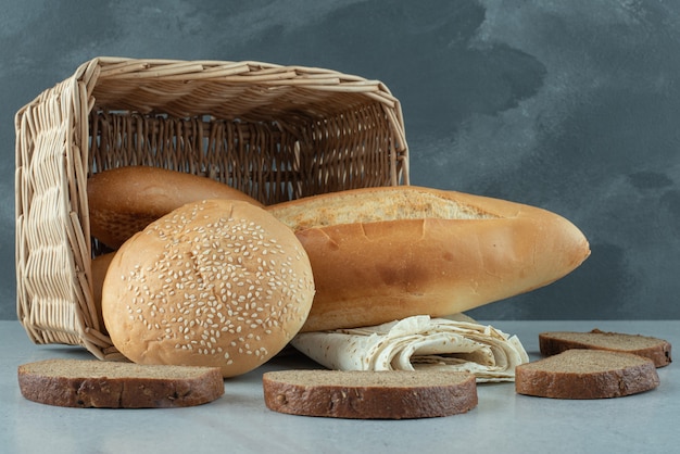 Variety of bread in basket and wheat on stone table