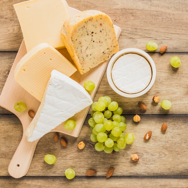 Variety of cheese blocks with grapes; almonds and chestnuts on wooden desk