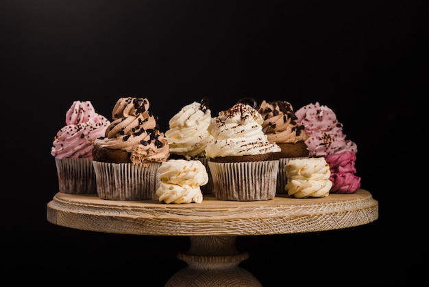 Variety of cupcakes on wooden cakestand against black background