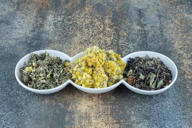 Variety of dried flowers and tea leaves in white bowls.