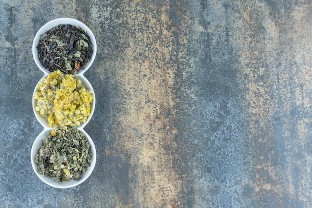 Variety of dried flowers and tea leaves in white bowls.