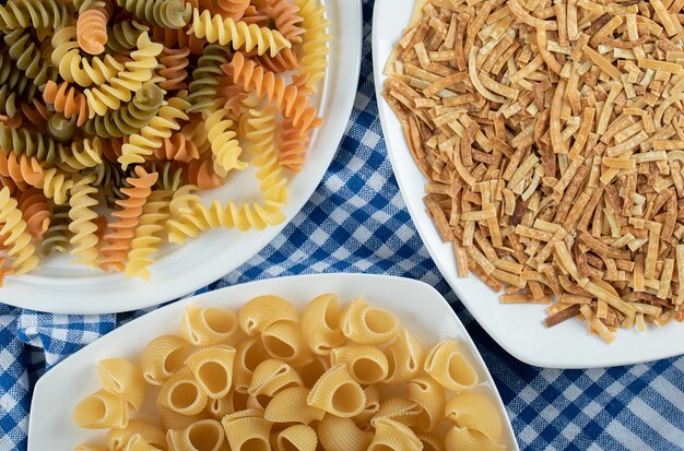 Variety of dry pasta on white plates with tablecloth.