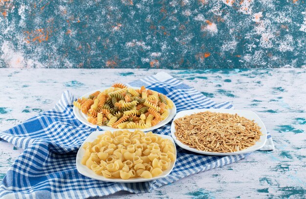 Variety of dry pasta on white plates with tablecloth.