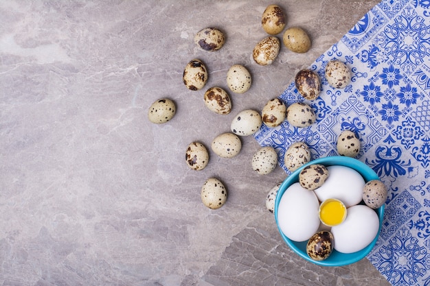 Variety of eggs in a blue cup and on ground.