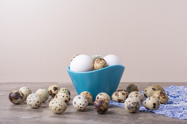 Variety of eggs in a blue cup and on the ground.