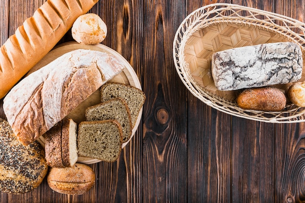 Разнообразие свежеиспеченного хлеба на плите и корзине над деревянным фоном