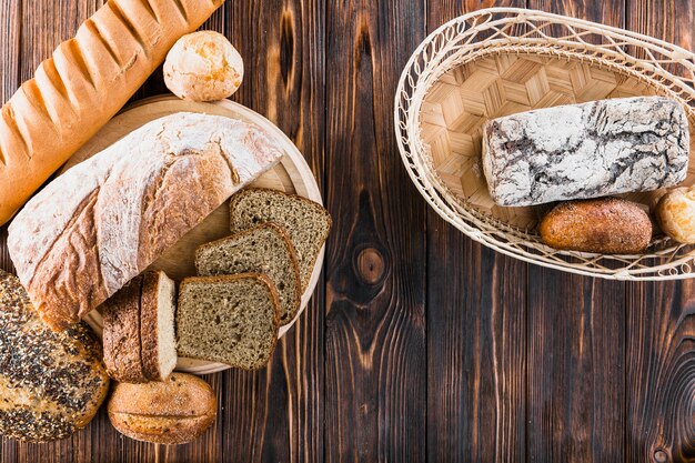 Variety of freshly baked breads on plate and basket over the wooden backdrop