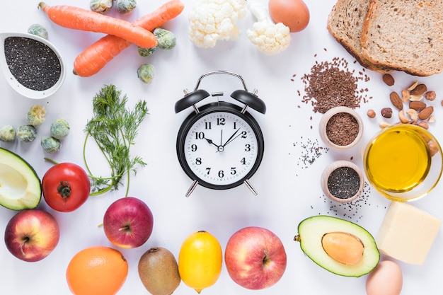 Variety of ingredients with alarm clock arranged against isolated on white background