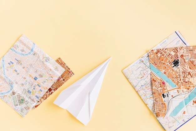 Variety of maps with white paper airplane on beige background