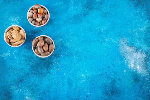 A variety of nuts in bowls , on the blue table. 