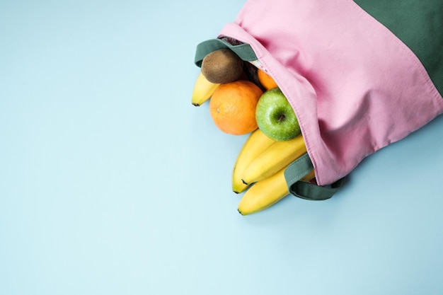 Разнообразие фруктов грейпфрут киви банан апельсин из розового льняного мешка на синем фоне вид сверху с пространством