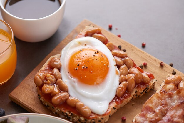 茶色の全粒粉パンにトマトソース、白豆、ベーコン、目玉焼きを添えたさまざまなオープンサンドイッチ。