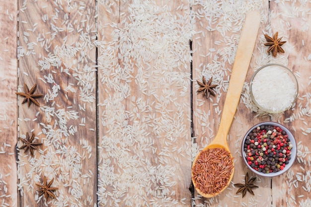 Variety of organic raw rice and tasty spices spread over wooden plank